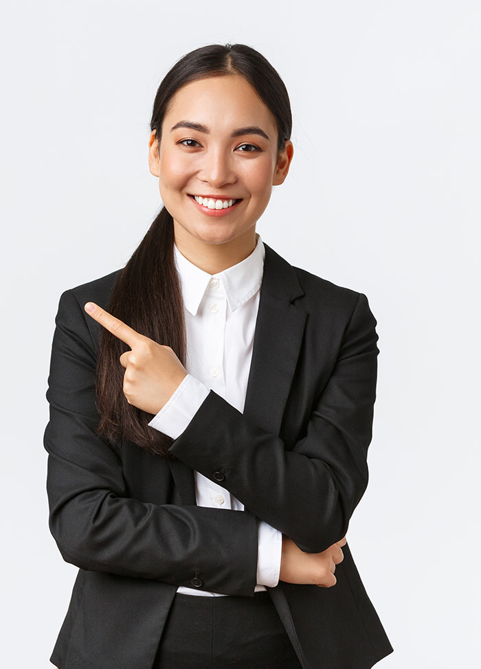 Happy professional asian female manager, businesswoman in suit showing announcement, smiling and pointing finger left at product or project banner, standing white background.
